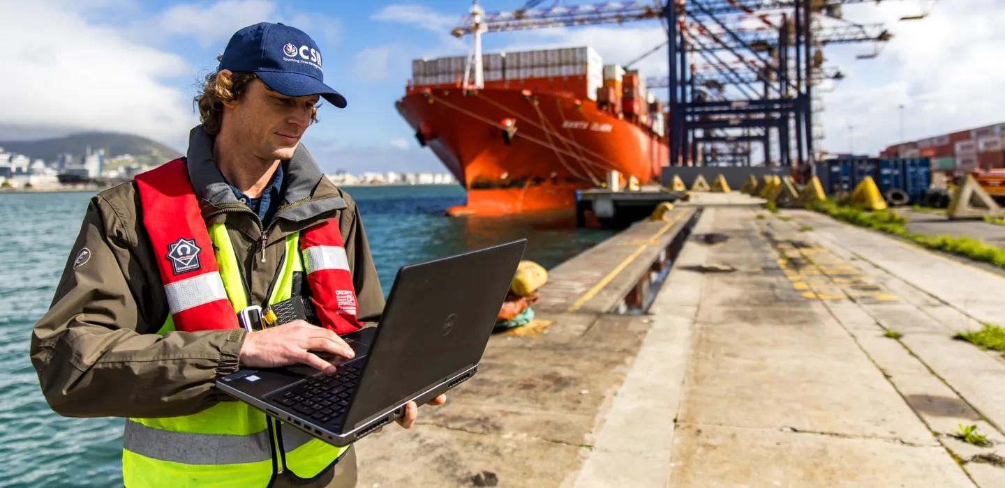 Man standing near a ship with his laptop